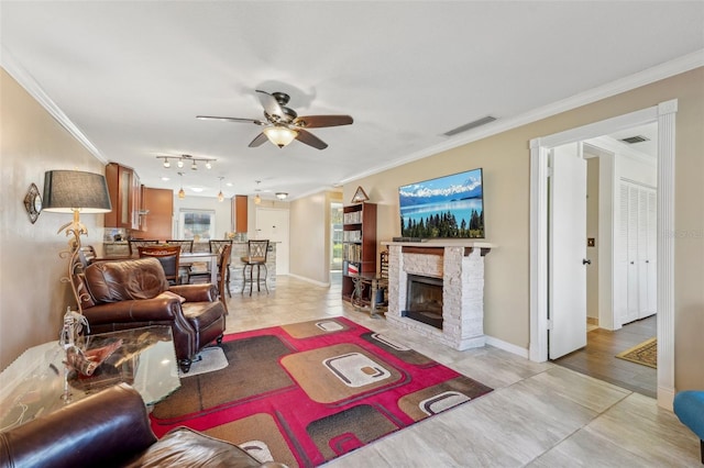 living room with light tile patterned floors, crown molding, a stone fireplace, and ceiling fan