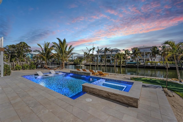 pool at dusk featuring an in ground hot tub, a water view, a patio, and pool water feature