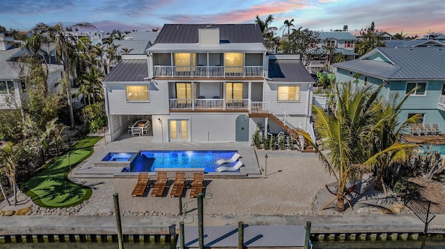 back house at dusk with a swimming pool with hot tub, a patio area, and a balcony