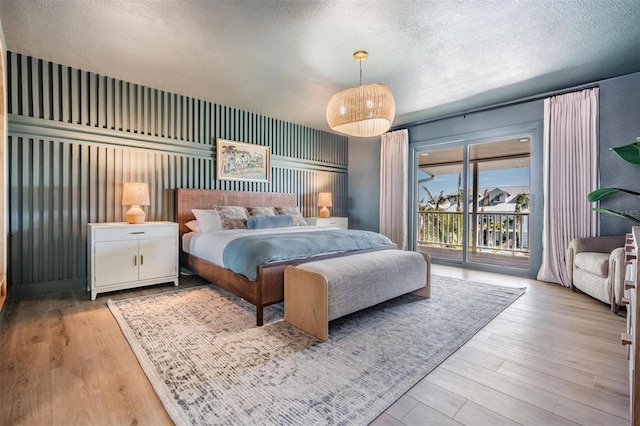 bedroom featuring access to exterior, light hardwood / wood-style floors, and a textured ceiling