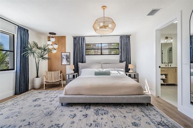 bedroom featuring ensuite bathroom, wood-type flooring, and a notable chandelier