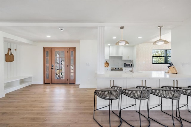 kitchen with light hardwood / wood-style flooring, kitchen peninsula, electric stove, decorative backsplash, and white cabinets