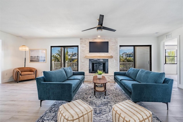 living room featuring a stone fireplace, ceiling fan, and light wood-type flooring