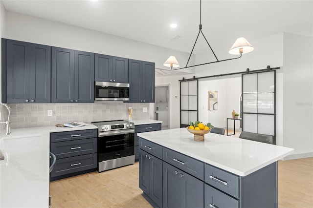 kitchen with sink, appliances with stainless steel finishes, hanging light fixtures, a center island, and a barn door