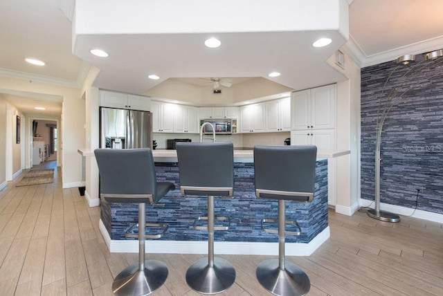 kitchen with appliances with stainless steel finishes, white cabinets, light hardwood / wood-style floors, crown molding, and a center island with sink