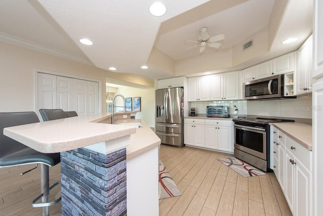 kitchen featuring sink, backsplash, stainless steel appliances, white cabinets, and a kitchen bar