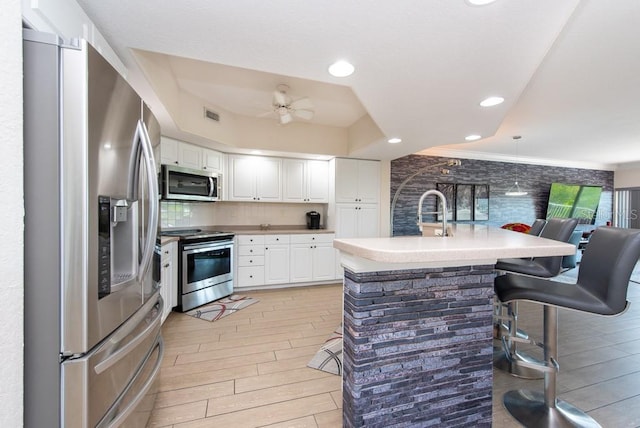 kitchen featuring a kitchen breakfast bar, ceiling fan, stainless steel appliances, decorative backsplash, and white cabinets