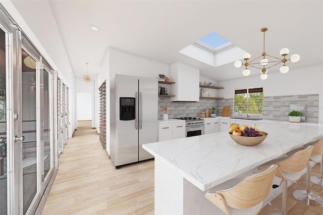 kitchen with lofted ceiling with skylight, appliances with stainless steel finishes, decorative light fixtures, white cabinets, and an inviting chandelier