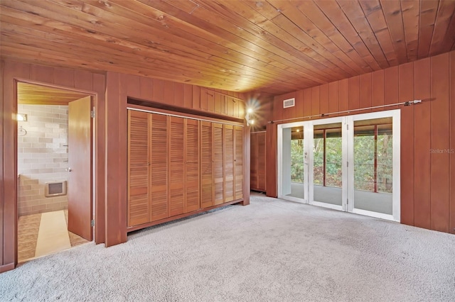 unfurnished bedroom with access to exterior, light colored carpet, wooden ceiling, and wooden walls