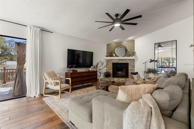 living room featuring vaulted ceiling, a stone fireplace, hardwood / wood-style floors, ceiling fan, and a textured ceiling