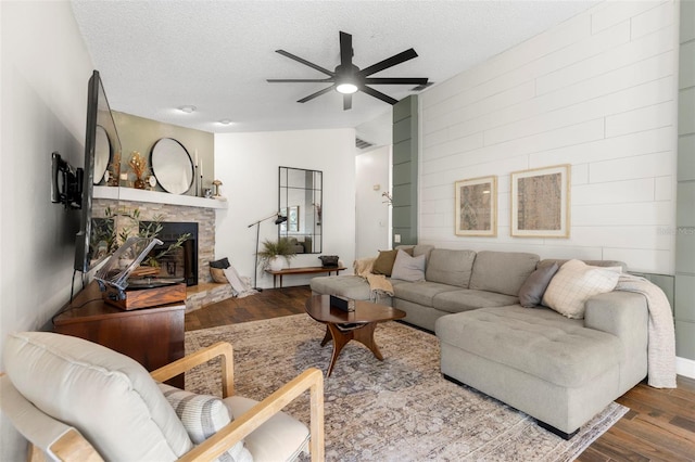 living room with hardwood / wood-style flooring, a stone fireplace, lofted ceiling, and a textured ceiling