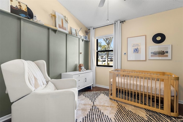 bedroom featuring a nursery area, ceiling fan, dark hardwood / wood-style floors, and a textured ceiling