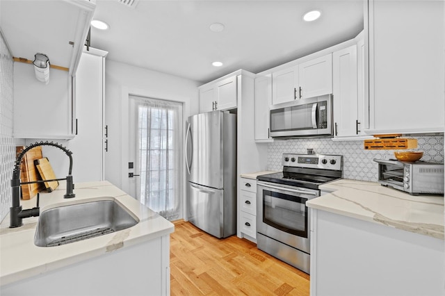 kitchen featuring tasteful backsplash, sink, white cabinets, stainless steel appliances, and light stone countertops