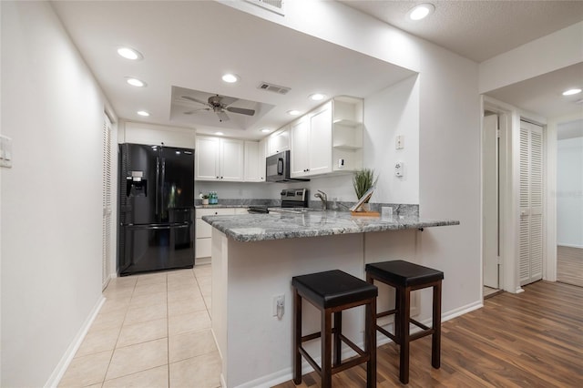 kitchen featuring light stone countertops, black appliances, kitchen peninsula, and white cabinets