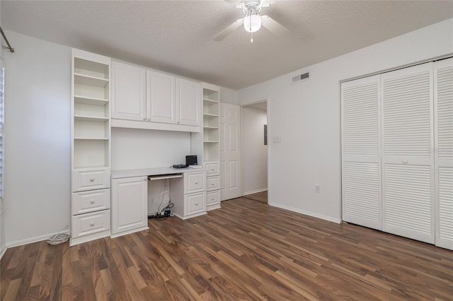 unfurnished office featuring ceiling fan, dark wood-type flooring, built in desk, and a textured ceiling