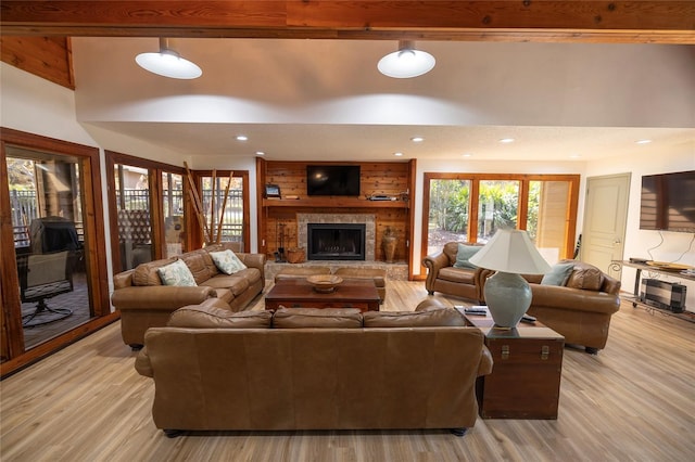 living room with a stone fireplace, light hardwood / wood-style floors, beamed ceiling, and a high ceiling