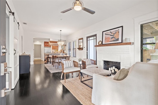 living room with dark wood-type flooring, ceiling fan, a barn door, and a fireplace