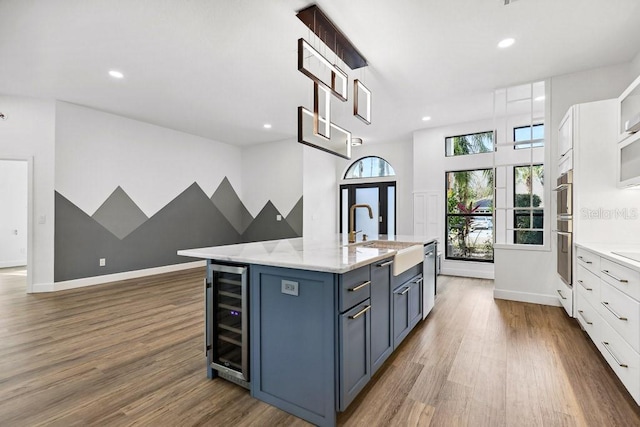 kitchen featuring sink, dark hardwood / wood-style flooring, an island with sink, beverage cooler, and white cabinets