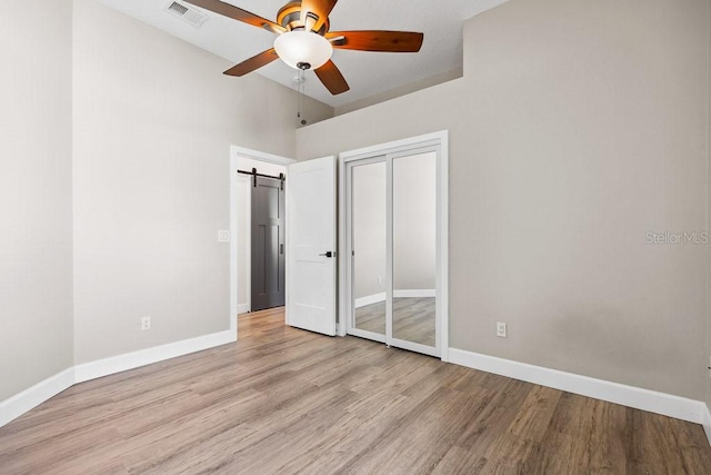 unfurnished bedroom featuring ceiling fan, a barn door, a closet, and light hardwood / wood-style flooring