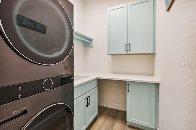 clothes washing area featuring light hardwood / wood-style floors, cabinets, and stacked washing maching and dryer