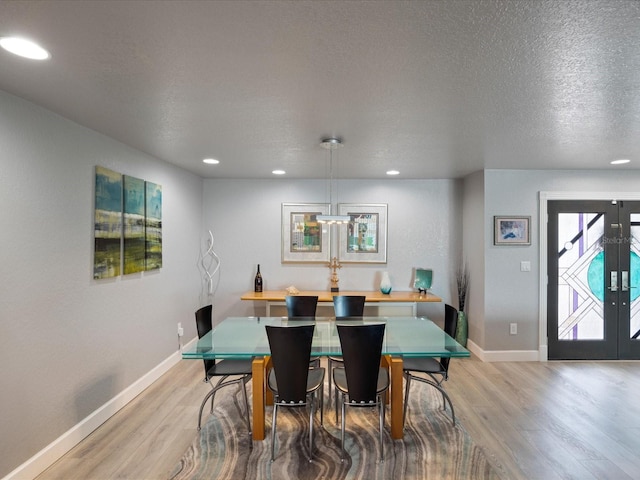 dining space with french doors, light hardwood / wood-style floors, and a textured ceiling