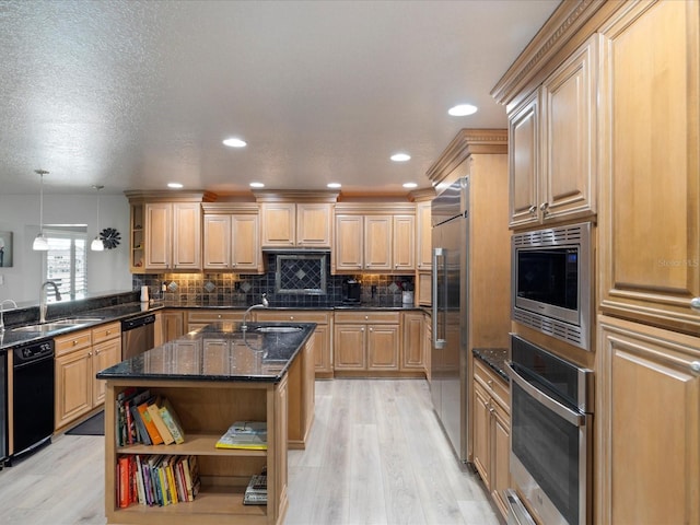 kitchen with sink, built in appliances, decorative light fixtures, kitchen peninsula, and dark stone counters