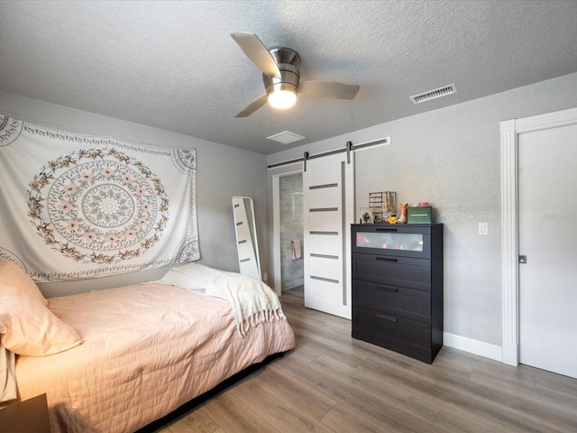 bedroom with ceiling fan, a barn door, hardwood / wood-style floors, and a textured ceiling