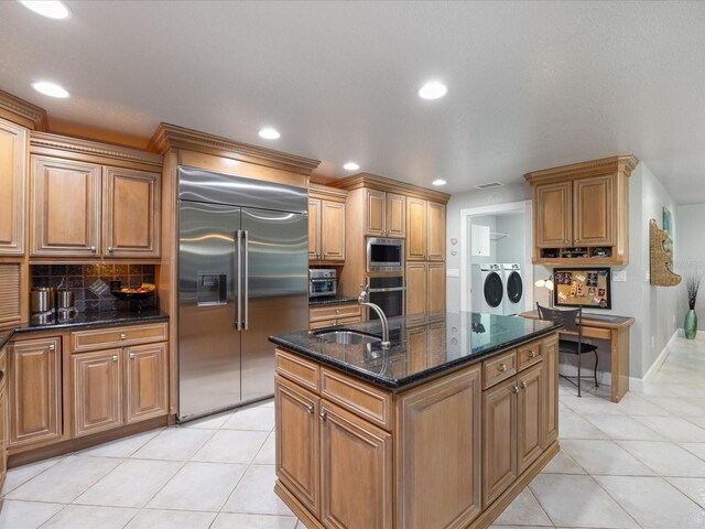 kitchen featuring washing machine and clothes dryer, sink, built in appliances, a center island with sink, and light tile patterned floors