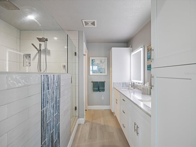 bathroom with vanity, wood-type flooring, a textured ceiling, and tiled shower