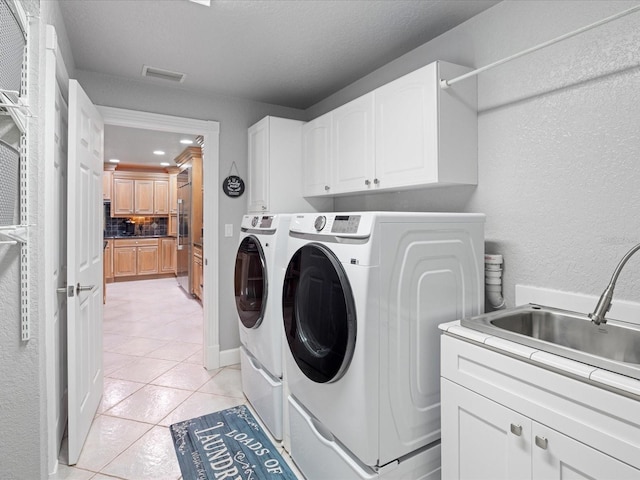 clothes washing area with washing machine and clothes dryer, sink, cabinets, a textured ceiling, and light tile patterned floors