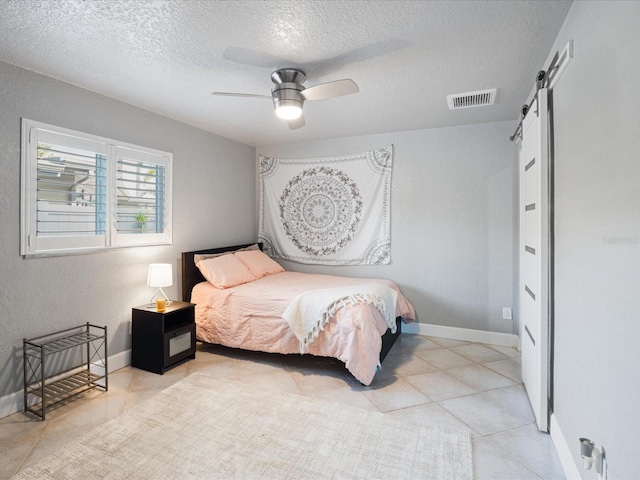 bedroom with light tile patterned floors, a textured ceiling, a barn door, and ceiling fan