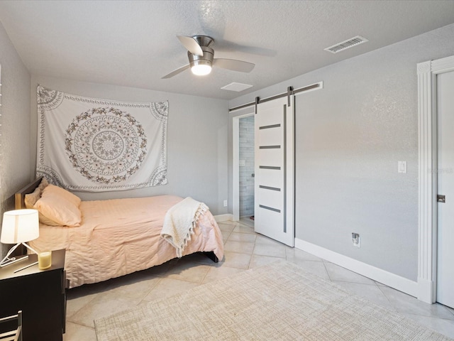 bedroom with light tile patterned flooring, a barn door, ceiling fan, and a textured ceiling