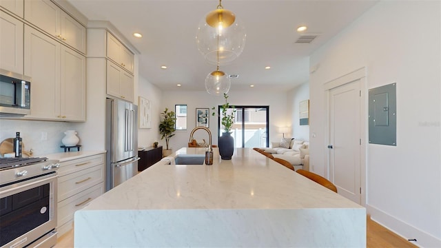 kitchen with sink, light stone counters, hanging light fixtures, electric panel, and stainless steel appliances