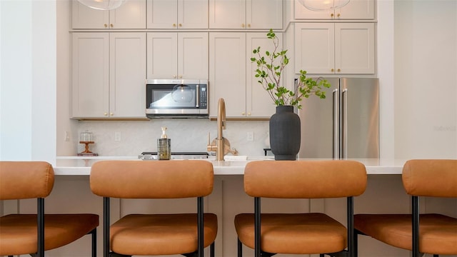 kitchen with appliances with stainless steel finishes, backsplash, white cabinets, and a kitchen bar