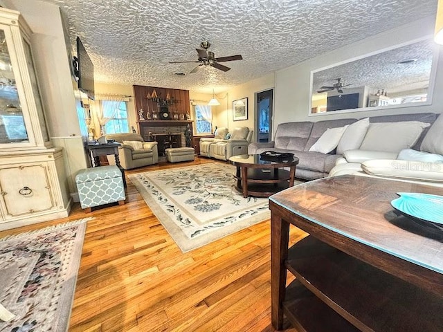 living room with ceiling fan, a textured ceiling, and light wood-type flooring