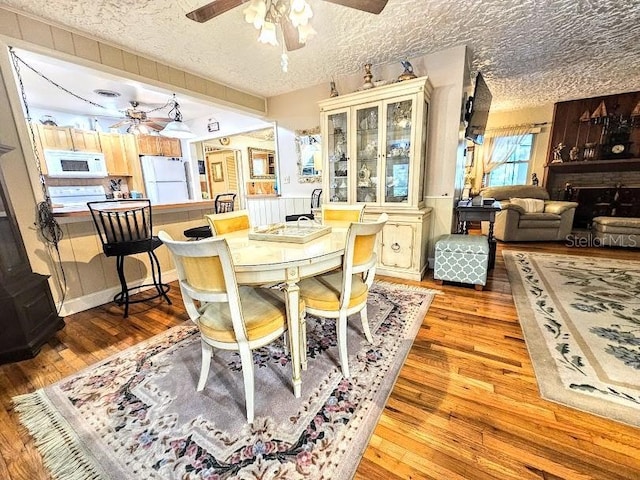 dining area featuring ceiling fan, light hardwood / wood-style floors, a large fireplace, and a textured ceiling