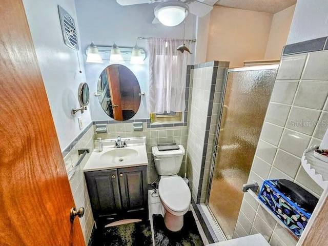 bathroom with ceiling fan, tile walls, vanity, toilet, and walk in shower