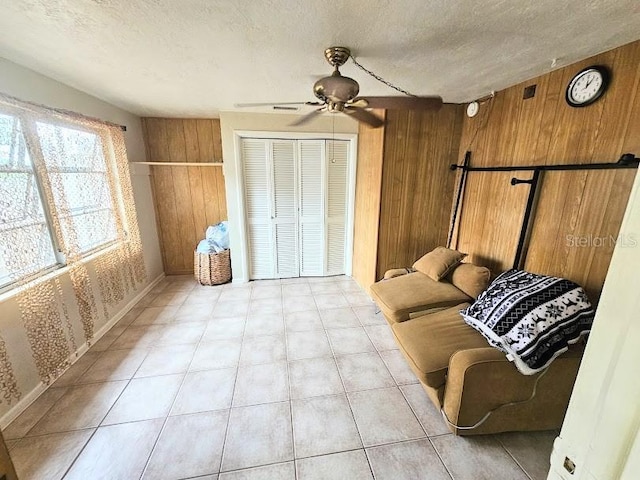 sitting room with ceiling fan, wooden walls, and a textured ceiling