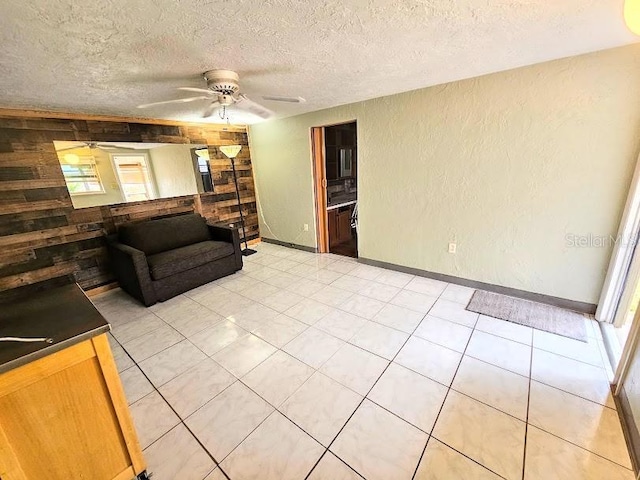 unfurnished living room featuring wooden walls, light tile patterned floors, a textured ceiling, and ceiling fan