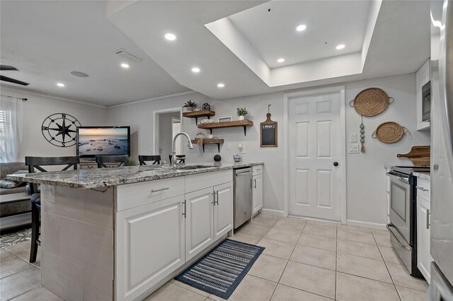 kitchen featuring a kitchen bar, sink, appliances with stainless steel finishes, light stone countertops, and white cabinets