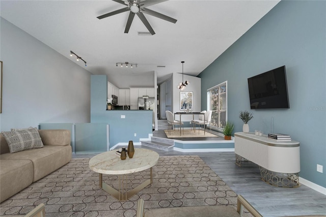 living room with ceiling fan with notable chandelier, track lighting, and light hardwood / wood-style flooring