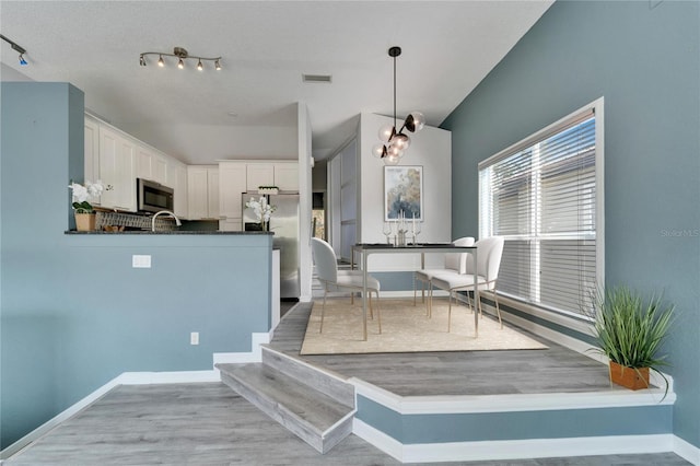 interior space featuring appliances with stainless steel finishes, an inviting chandelier, light hardwood / wood-style floors, white cabinets, and decorative light fixtures