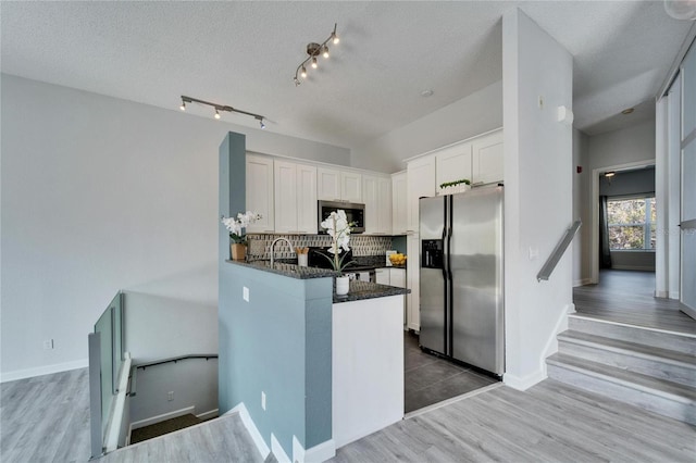 kitchen with tasteful backsplash, appliances with stainless steel finishes, kitchen peninsula, hardwood / wood-style floors, and white cabinets