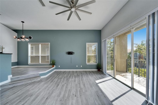 empty room featuring ceiling fan with notable chandelier and light wood-type flooring