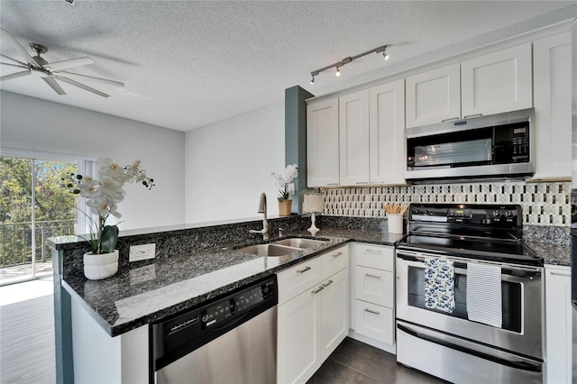 kitchen featuring appliances with stainless steel finishes, white cabinetry, sink, dark stone counters, and kitchen peninsula