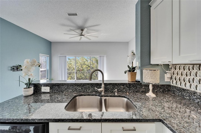 kitchen with dishwasher, white cabinetry, sink, dark stone countertops, and a textured ceiling