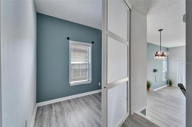 hallway with a chandelier, light hardwood / wood-style flooring, and a textured ceiling