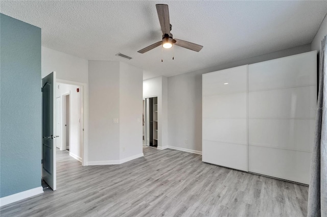 empty room with ceiling fan, a textured ceiling, and light wood-type flooring