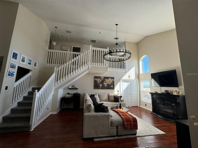 living room with dark wood-type flooring, high vaulted ceiling, an inviting chandelier, and a textured ceiling