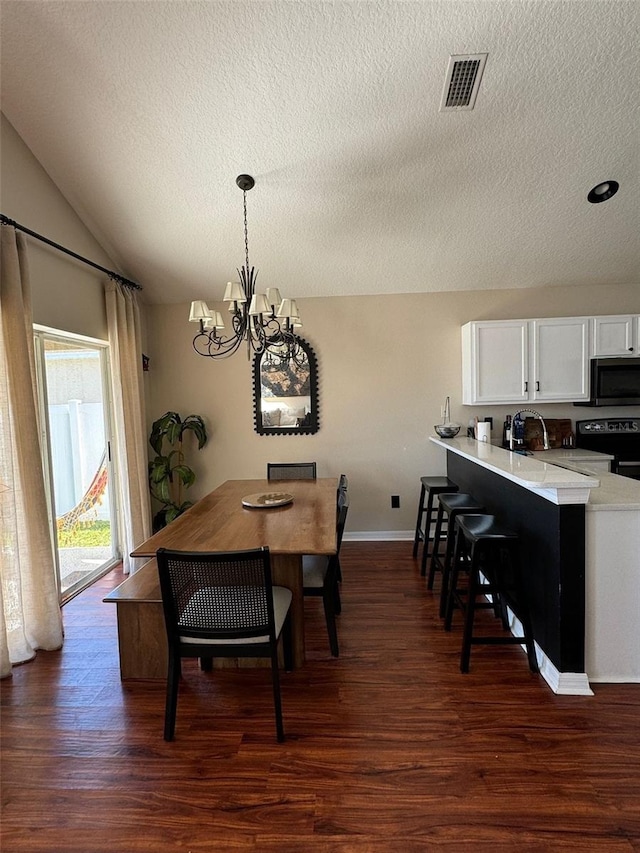 dining area featuring lofted ceiling, dark hardwood / wood-style floors, a chandelier, and a textured ceiling